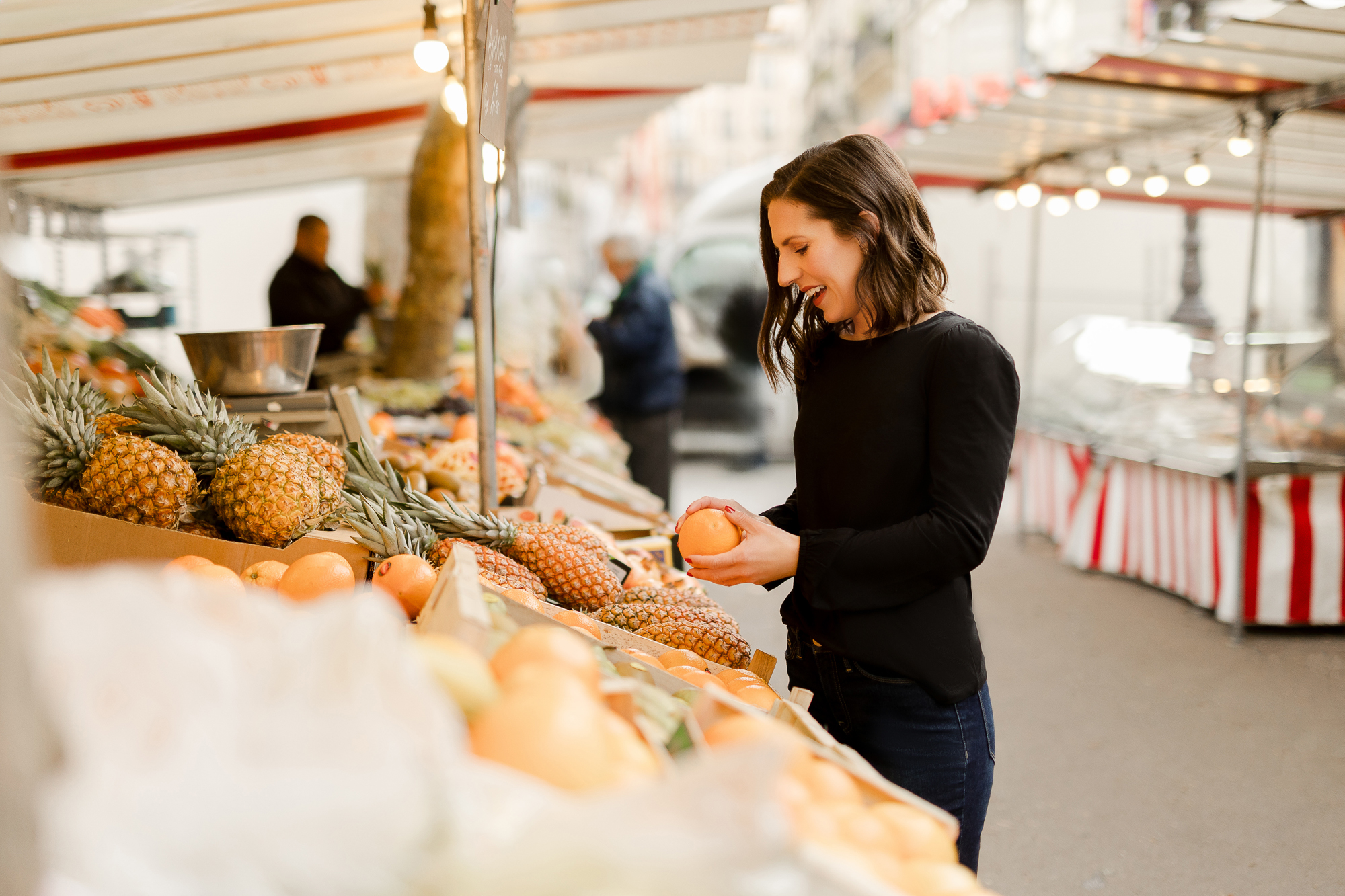 Portrait of woman at outdoor market in Paris holding oranges by Katie Donnelly Photography