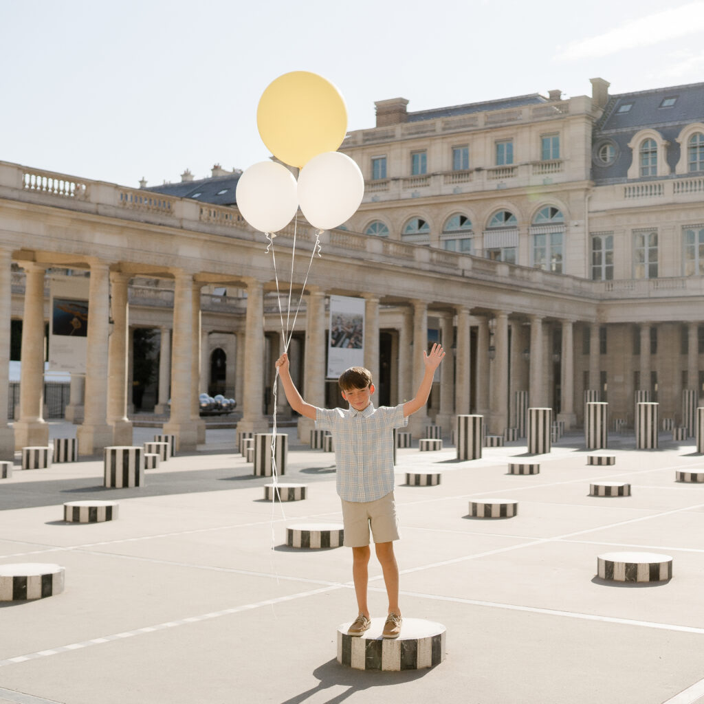 Portrait of boy holding balloons at Palais Royal in Paris in summer by Katie Donnelly Photography