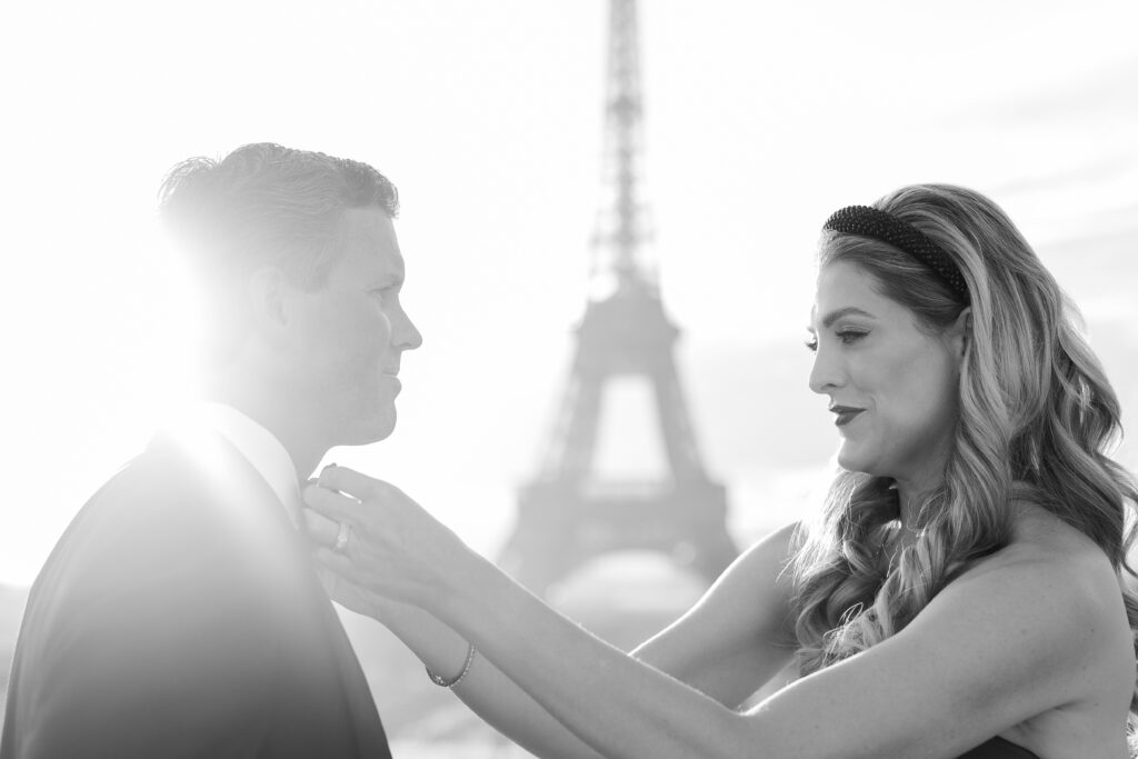 Black and white portrait of woman adjusting tie on man in romantic scene with Eiffel Tower by Katie Donnelly Photography