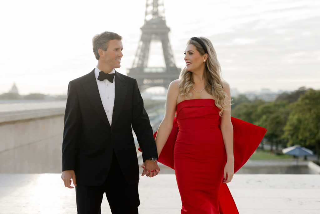 Romantic Color Portrait of couple in tuxedo and red gown holding hands with Eiffel Tower in the background of Paris by Katie Donnelly Photography