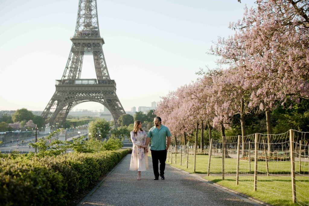 Portrait of couple walking near flowering trees and Eiffel Tower during Spring flower blossoms in Paris by Katie Donnelly Photography