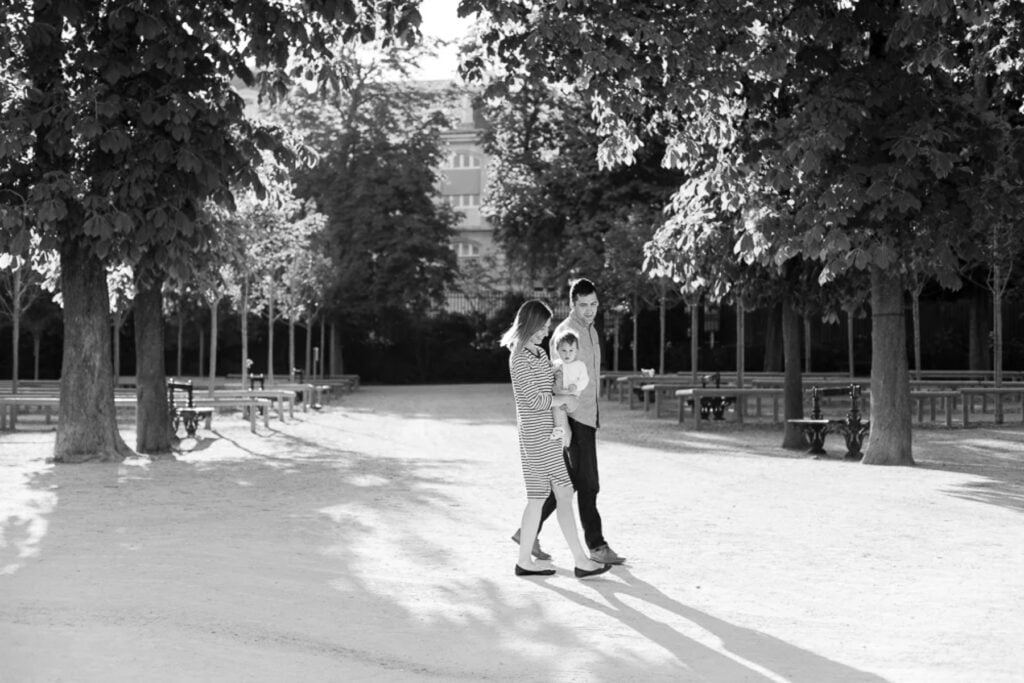 Black and white photo of parents walking with their baby under the trees in the Luxembourg Gardens
