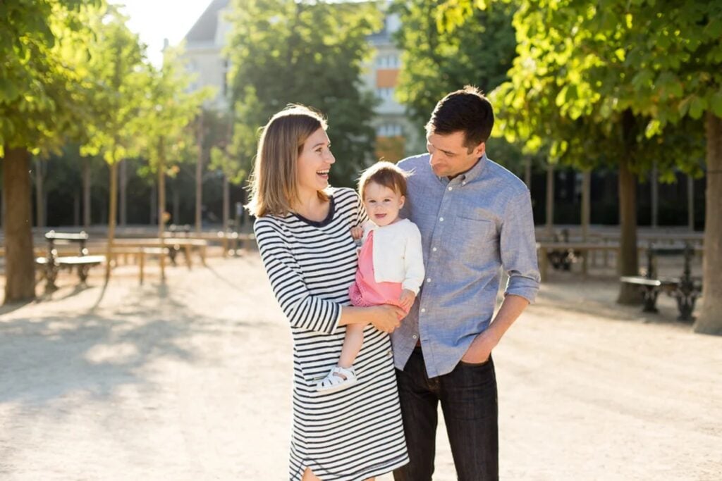 Parents in navy stripes and chambray holding their baby in a pink romper in a Paris garden
