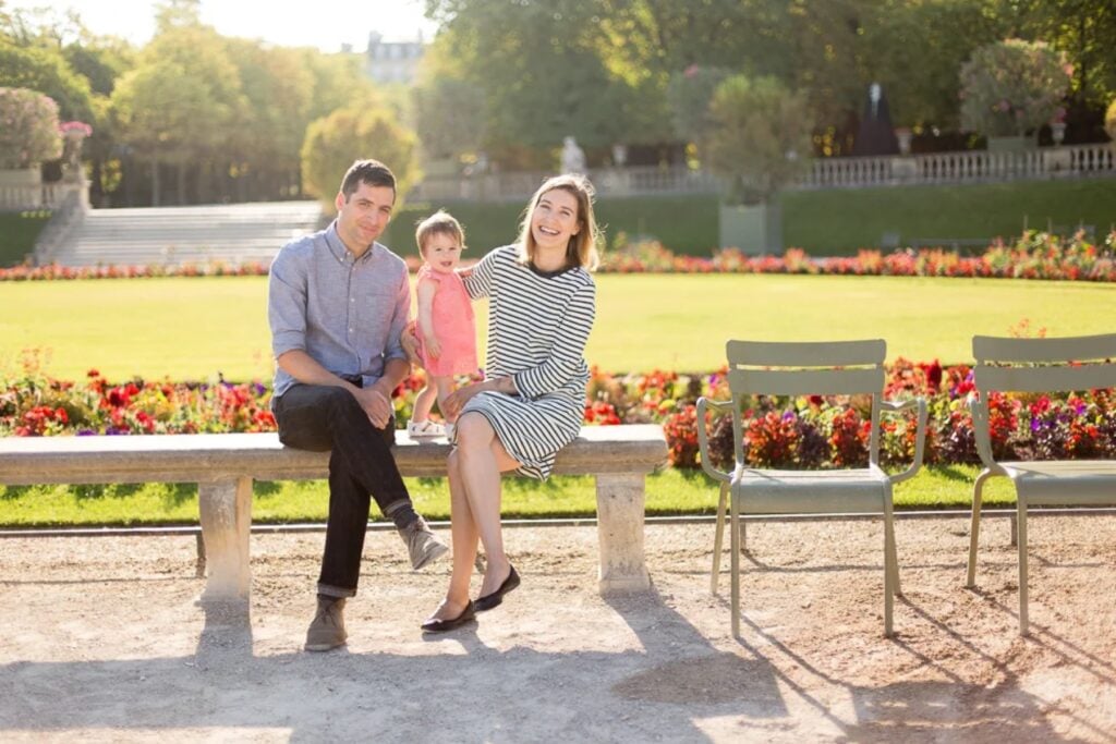 Family sitting on a bench in front of the flower beds in the Luxembourg Gardens