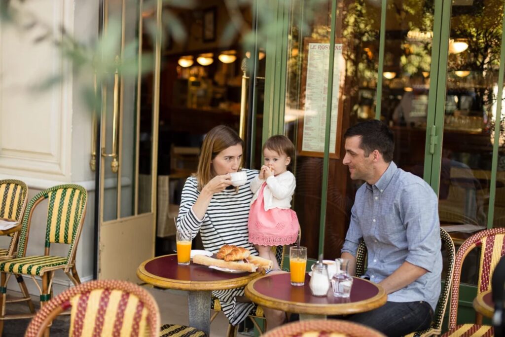 Family of three sitting at a Paris café terrace with wicker chairs