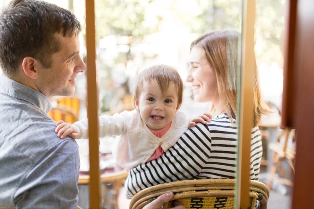 Parents and baby laughing together at a café table in Paris