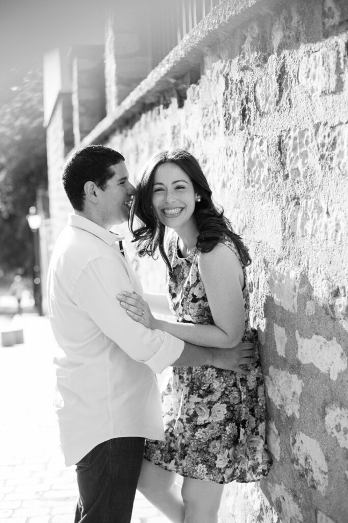 Black and white photo of a couple laughing against a stone wall during a morning photoshoot in Paris