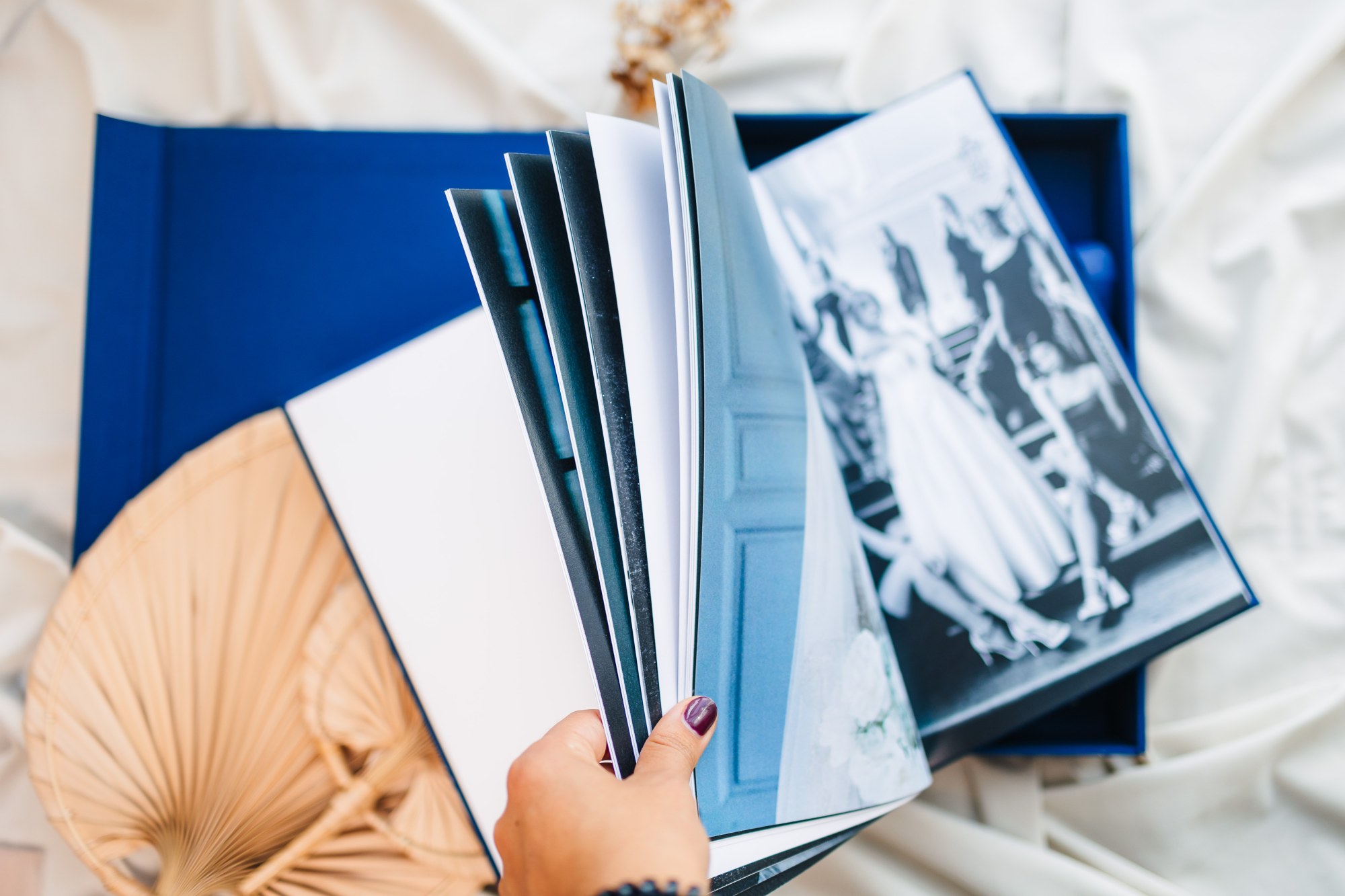 Hand fanning through the pages of an heirloom photo album above its blue presentation box