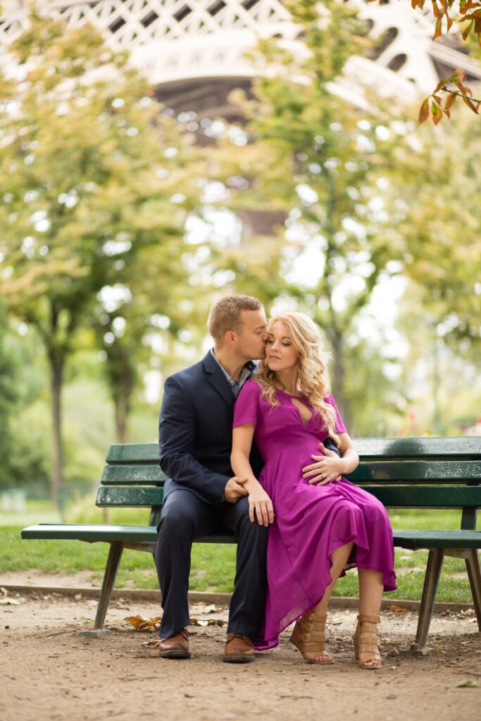 Expecting couple cuddling on a green park bench under the Eiffel Tower during a Paris maternity photoshoot