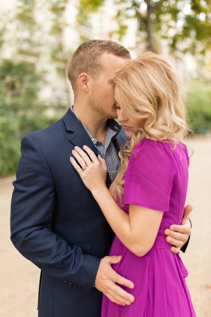 Dad-to-be holding his pregnant wife in a magenta dress in a Paris garden near the Eiffel Tower