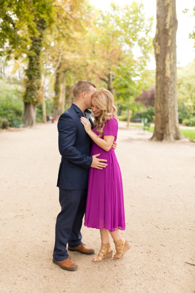 Expecting couple kissing on a tree-lined path near the Eiffel Tower in Paris