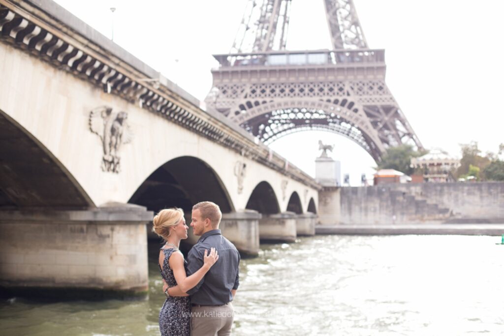 Couple kissing on the bank of the Seine with a stone bridge and the Eiffel Tower behind them