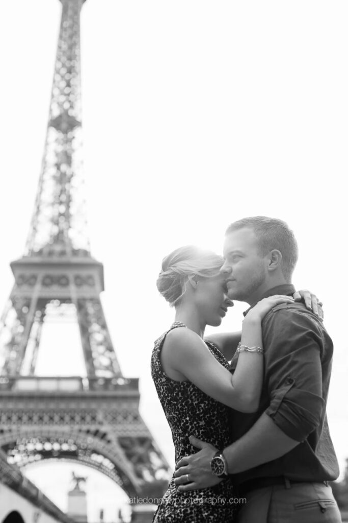 Black and white photo of a couple touching foreheads beside the Eiffel Tower