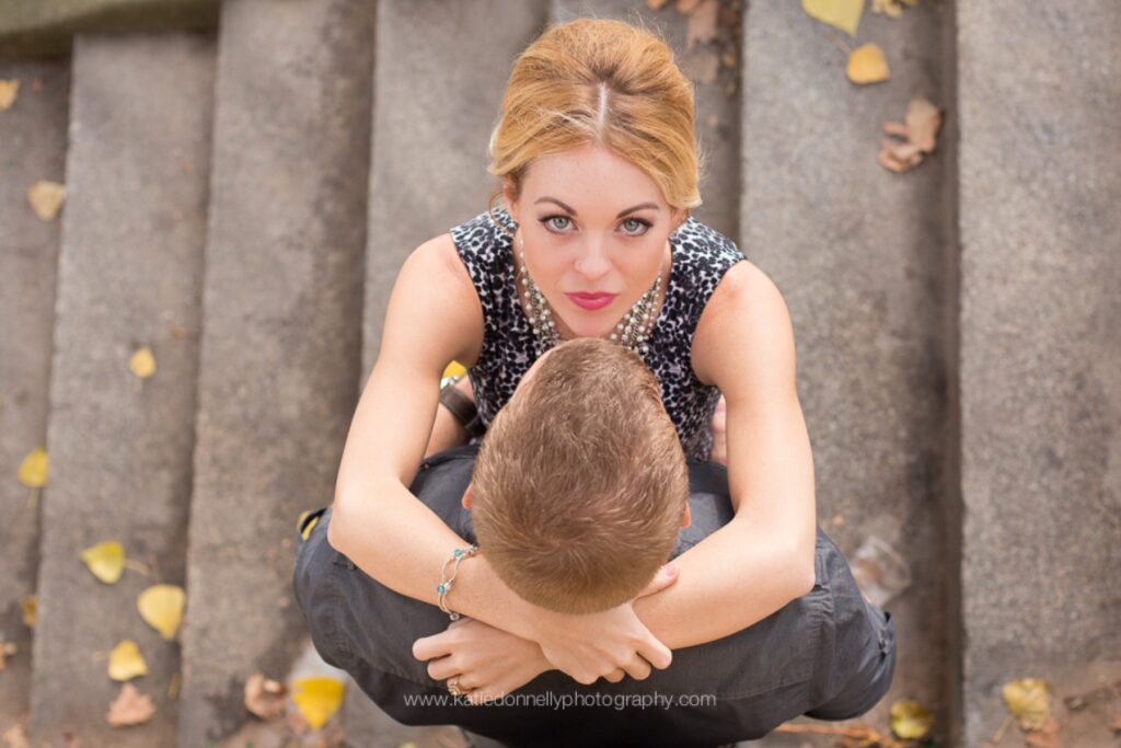 Couple seen from above sitting together on stone steps scattered with autumn leaves