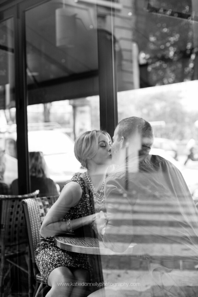 Black and white photo of a couple laughing at a Paris café, seen through the window