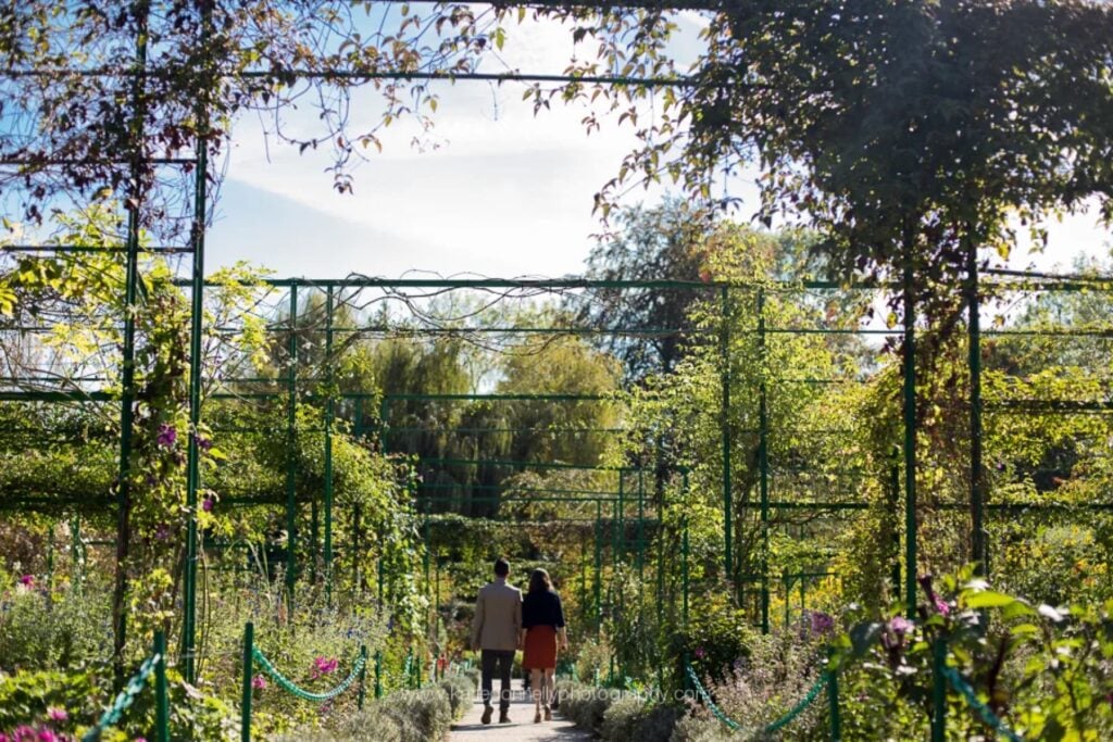 Couple walking under the rose arches of Monet's garden in Giverny before a surprise proposal