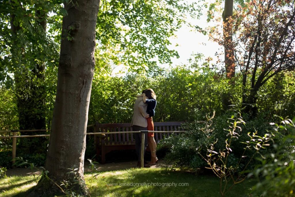 Newly engaged couple hugging by a bench under the trees in Monet's garden, Giverny