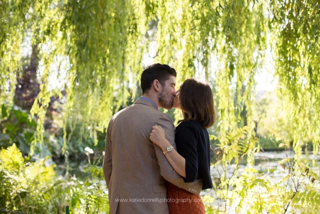 Couple kissing under a weeping willow by the water lily pond in Monet's garden