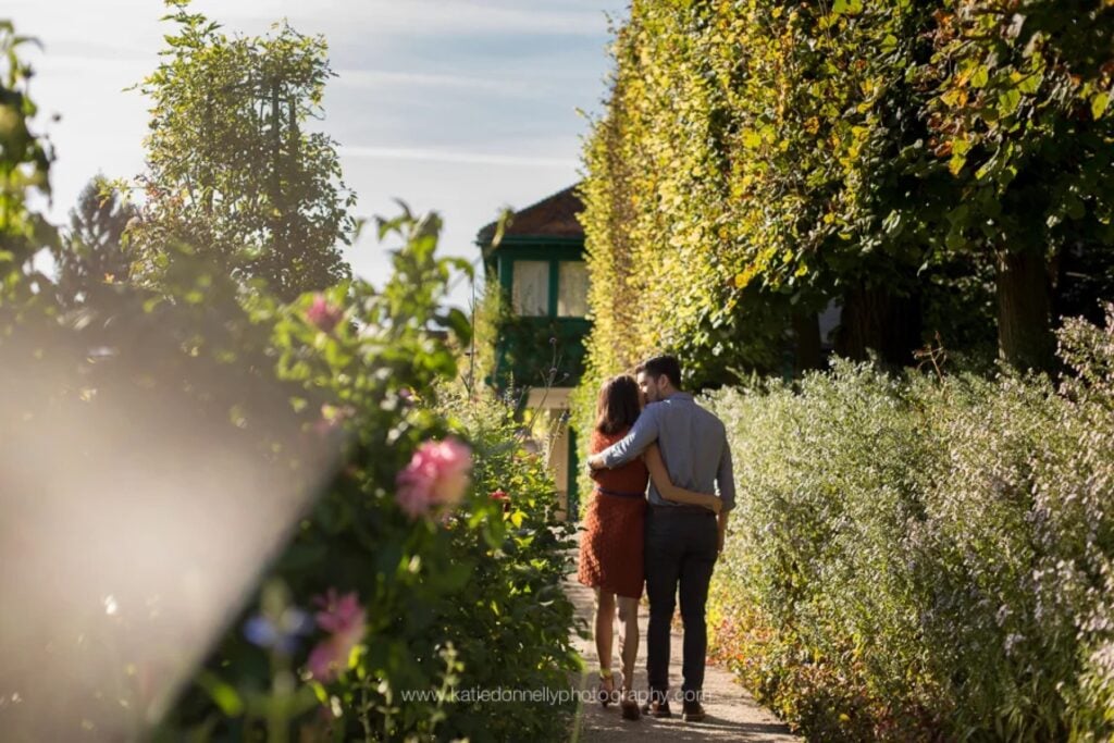 Engaged couple walking arm in arm along a flower-lined path toward Monet's house in Giverny