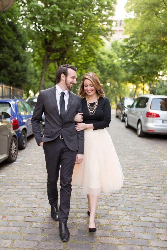 Couple walking arm in arm down a cobblestone street near the Eiffel Tower, she in a blush tulle skirt