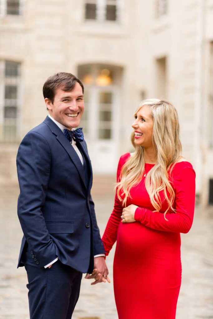 Expecting couple holding hands on a Paris street, mom-to-be in a red maternity dress
