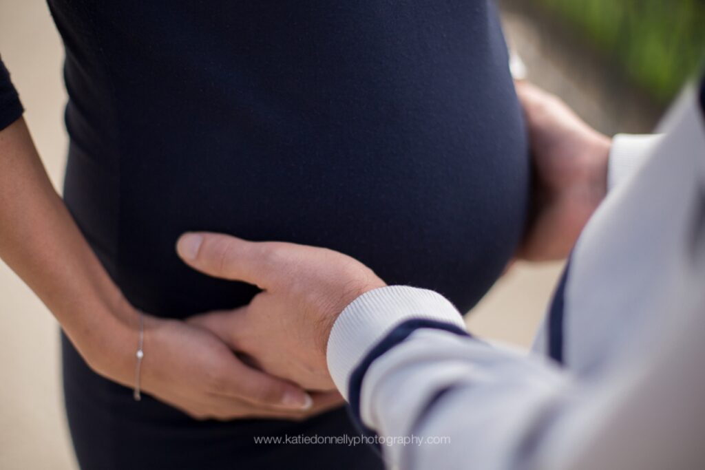 Close-up of an expecting couple's hands on her baby bump in a navy dress