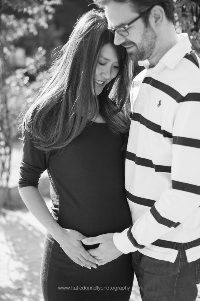 Black and white photo of an expecting couple leaning together, his hand on her baby bump