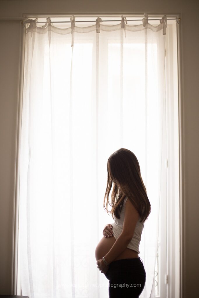 Silhouette of a pregnant woman standing at a tall Parisian window