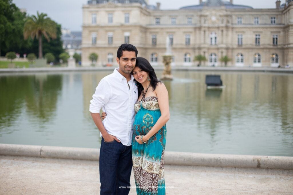 Expecting couple standing by the pond in front of the Luxembourg Palace during a Paris maternity photoshoot
