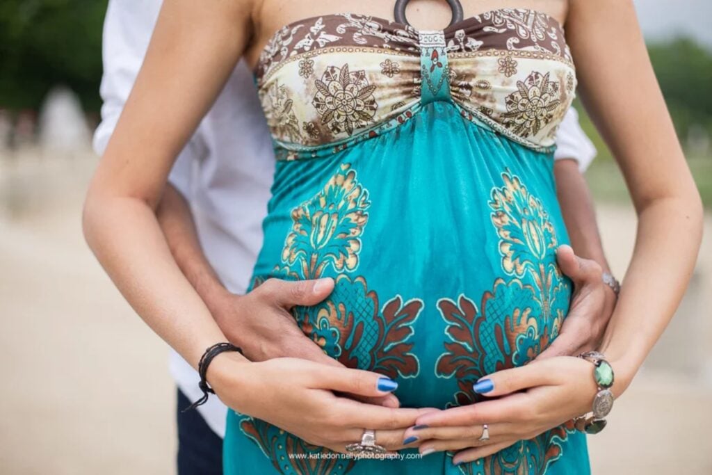 Close-up of an expecting couple's hands on her baby bump in a turquoise dress