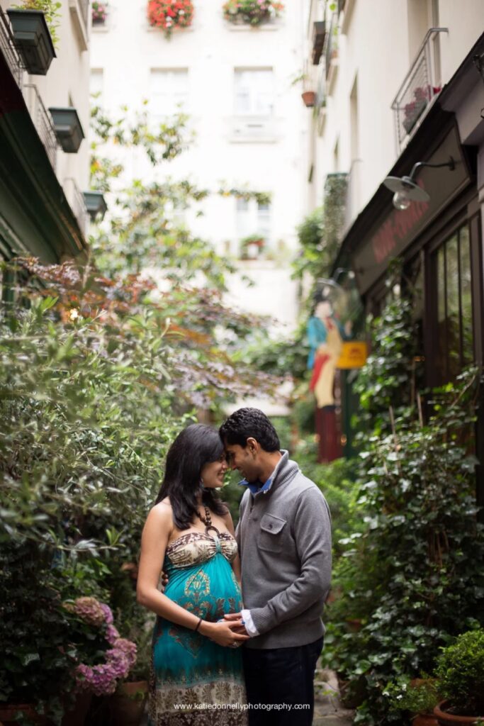 Expecting couple embracing in a leafy Paris passage during a rainy day maternity session