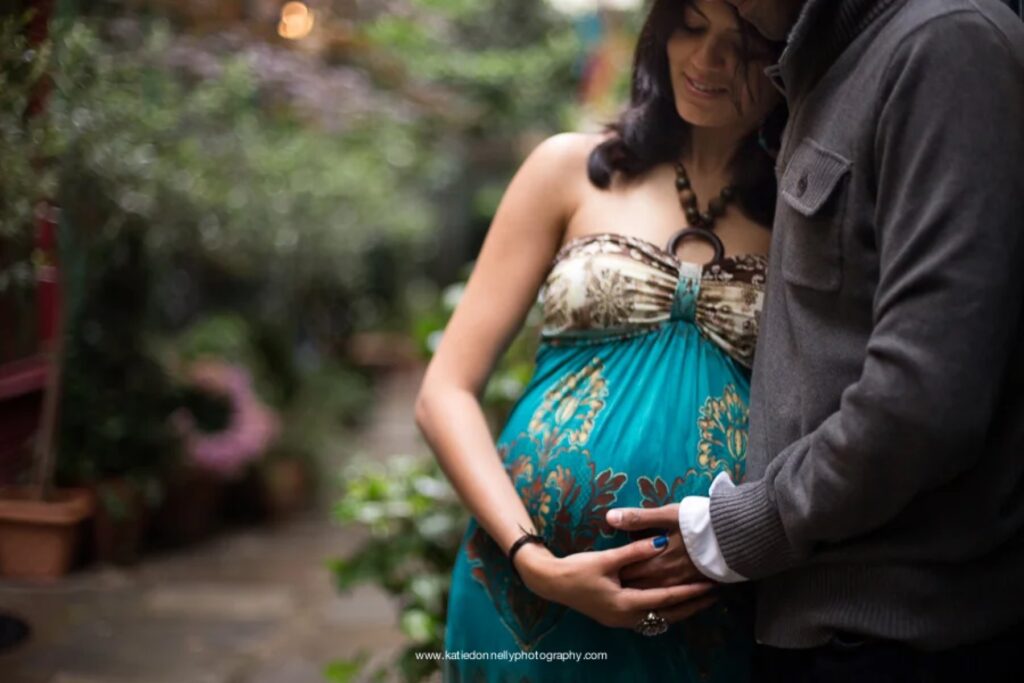 Close-up of an expecting couple holding her baby bump among green plants