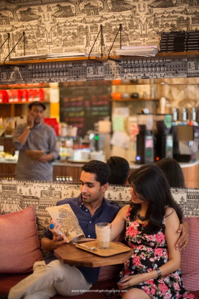 Expecting couple sharing a drink on a pink sofa inside a coffee shop in the Marais, Paris