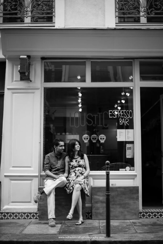 Black and white photo of an expecting couple sitting on the step outside a Paris coffee shop