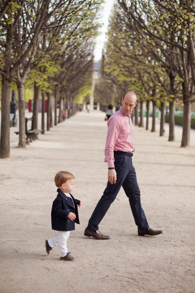Dad and toddler son walking down a tree-lined alley in the Palais Royal gardens