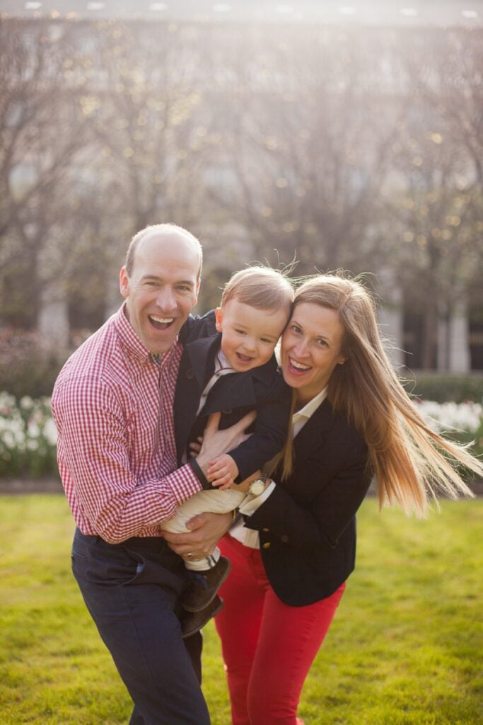 Parents laughing as they hold their toddler son on the lawn at the Palais Royal