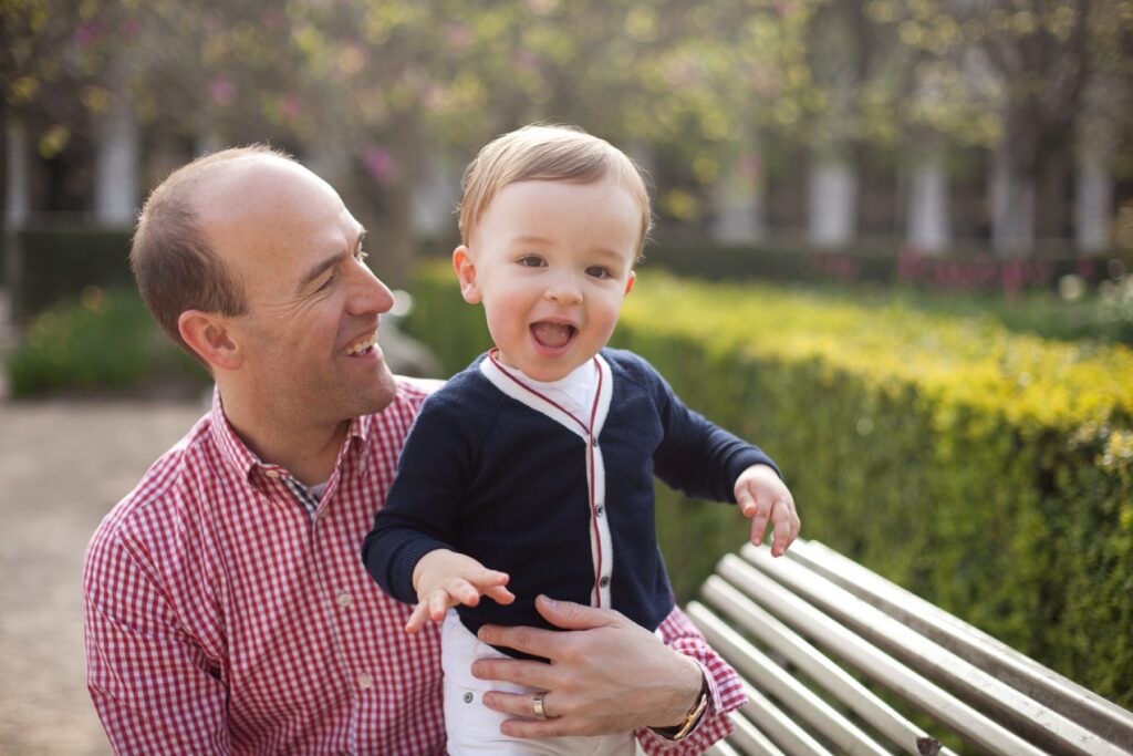 Dad holding his excited toddler son on a garden bench