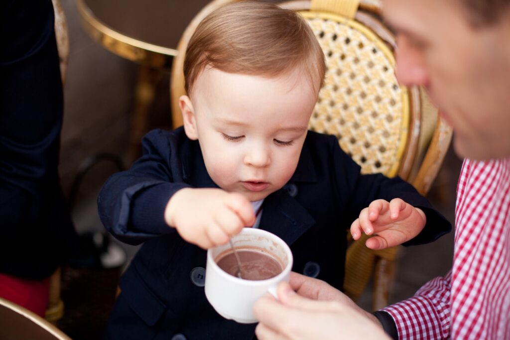 Toddler boy tasting hot chocolate at a Paris café with his dad
