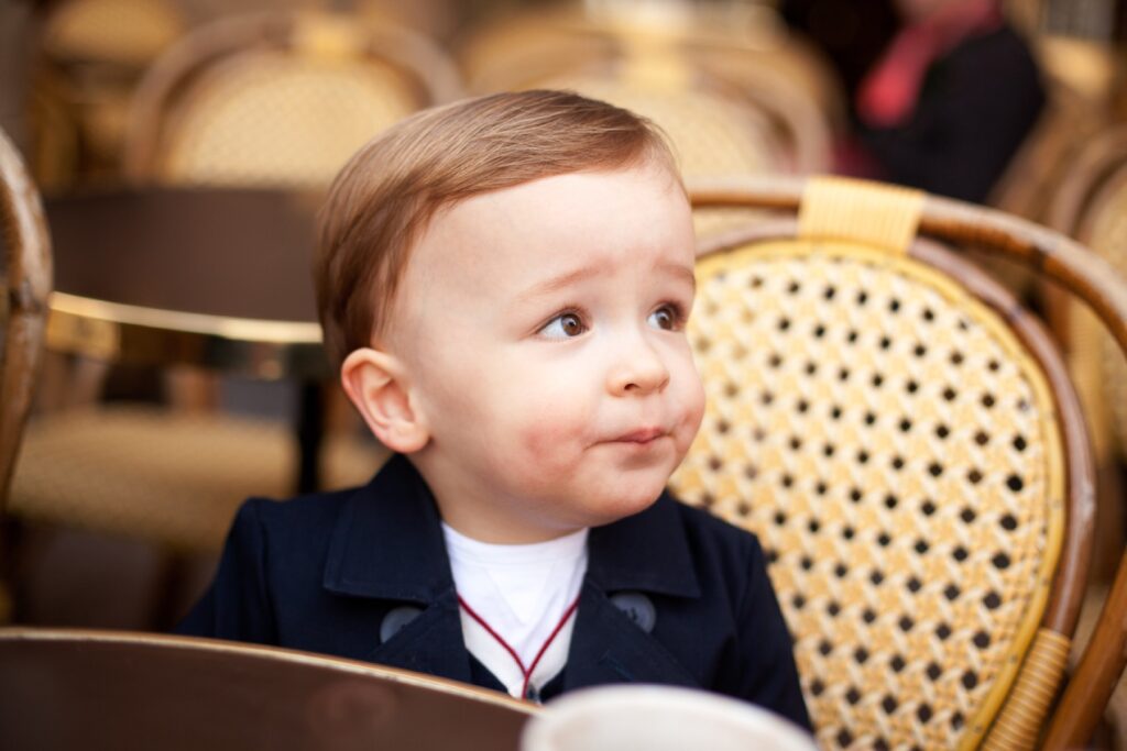 Toddler boy with a chocolate moustache sitting in a wicker café chair in Paris