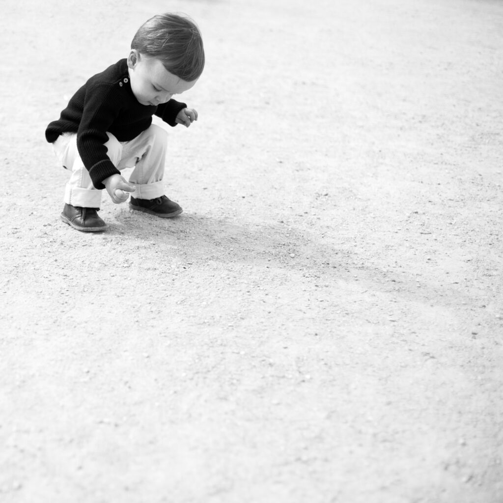 Black and white photo of a toddler bending down to look at the gravel path