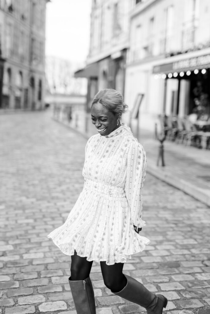 Black and white portrait of a woman laughing as she walks across the cobblestones at Place Dauphine during a solo photoshoot in Paris