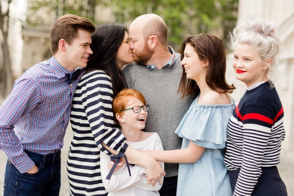 Family with three teenagers and a younger son hugging and laughing during a family photoshoot in Paris