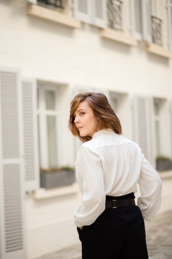 Woman in a white blouse looking over her shoulder on a quiet Paris street during a solo portrait session